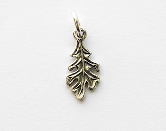 May include: A small, silver-toned metal charm shaped like an oak leaf with detailed, raised veins and scalloped edges. The charm features a circular jump ring attached to the top, allowing it to be suspended from a chain or other jewelry component.