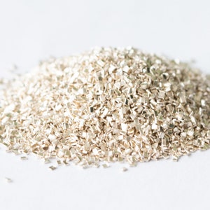 May include: A pile of small, silver-coloured metal flakes on a white background.