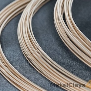 May include: Close-up of multiple spools of gold-colored wire. The wire is arranged in a circular pattern, with the ends of the wire overlapping.