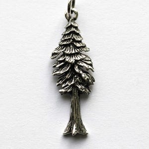 Op de afbeelding: Een zilverkleurige hanger in de vorm van een gedetailleerde groenblijvende boom. De hanger heeft een getextureerde stam en gelaagde, getextureerde takken. De boom hangt aan een kleine, cirkelvormige balein. De achtergrond is effen wit.