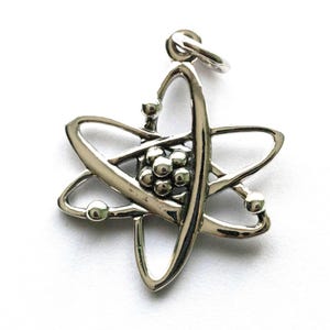 K&ouml;nnte beinhalten: Ein silberfarbener Atom-Anh&auml;nger. Der Anh&auml;nger zeigt eine zentrale Ansammlung von Kugeln, die von umlaufenden Schleifen und Kugeln umgeben sind, alle verbunden mit einer Schlaufe zum Aufh&auml;ngen. Das Design ist detailliert und hat eine polierte Oberfl&auml;che.