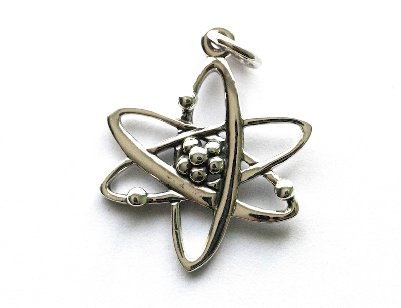 K&ouml;nnte beinhalten: Ein silberfarbener Atom-Anh&auml;nger. Der Anh&auml;nger zeigt eine zentrale Ansammlung von Kugeln, die von umlaufenden Schleifen und Kugeln umgeben sind, alle verbunden mit einer Schlaufe zum Aufh&auml;ngen. Das Design ist detailliert und hat eine polierte Oberfl&auml;che.