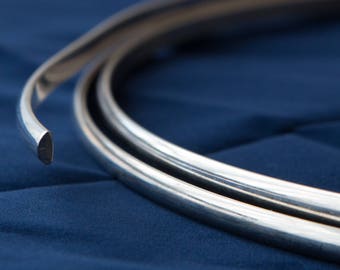 May include: A close-up of a silver metal trim, coiled and ready for use. The trim is shiny and has a smooth, rounded edge.