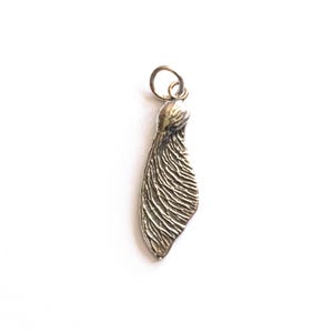 Könnte beinhalten: Ein detaillierter, silberfarbener Anhänger in Form eines Ahornsamens mit aufwendigen strukturierten Linien. Der Anhänger hat oben eine kleine Schlaufe zum Befestigen an einer Kette oder einem Armband. Das Design ist von der Natur inspiriert.