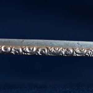 Könnte beinhalten: Nahaufnahme eines silberfarbenen Metallobjekts mit einem komplizierten, verzierten Design. Das Design zeigt ein sich wiederholendes Muster aus Wirbeln und Kurven.