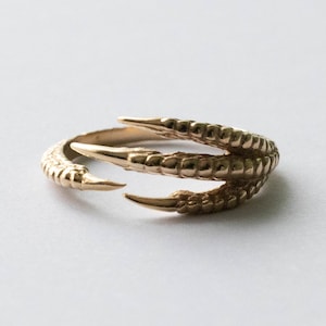 May include: A gold-toned ring shaped like a bird's claw with three talons.