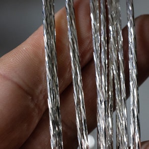 Könnte beinhalten: Nahaufnahme von mehreren silberfarbenen, gedrehten Drahtsträngen. Der Draht ist glänzend und hat eine strukturierte Oberfläche.