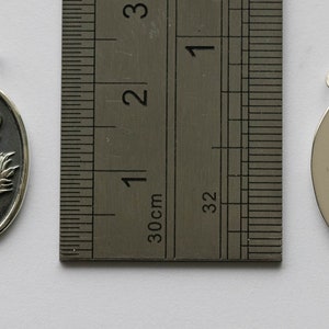 May include: Two silver oval pendants, one with a detailed embossed design of a flower and the other plain. The pendants are approximately 2 cm in length.
