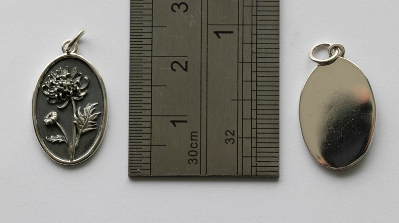 May include: Two silver oval pendants, one with a detailed embossed design of a flower and the other plain. The pendants are approximately 2 cm in length.