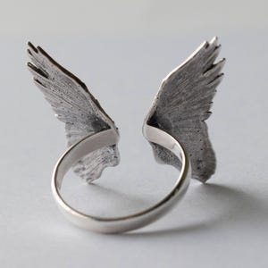 Peut inclure: Une bague en argent avec deux ailes de chaque c&ocirc;t&eacute;. Les ailes sont d&eacute;taill&eacute;es et textur&eacute;es.