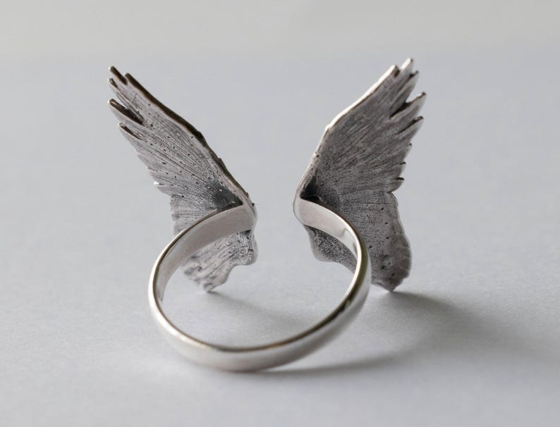 Peut inclure: Une bague en argent avec deux ailes de chaque c&ocirc;t&eacute;. Les ailes sont d&eacute;taill&eacute;es et textur&eacute;es.