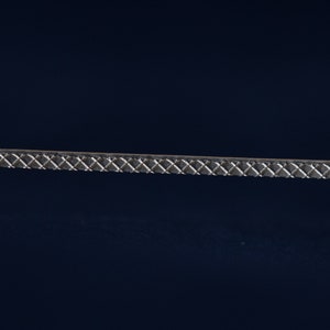 Może przedstawiać: Zbliżenie srebrnej, fakturowanej, ozdobnej listwy. Listwa ma wzór diamentowy.