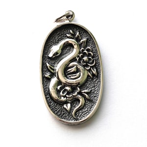 May include: Silver oval pendant with a detailed design of a snake entwined with flowers and leaves. The pendant has a textured background and a small loop for a chain. The snake is the central element, its body forming graceful curves.