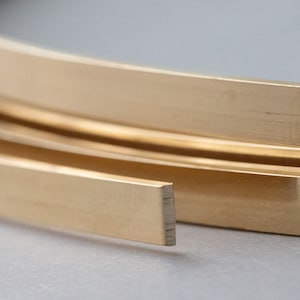 May include: A close-up of a coil of gold-colored metal trim. The trim is flat and has a smooth, polished finish.