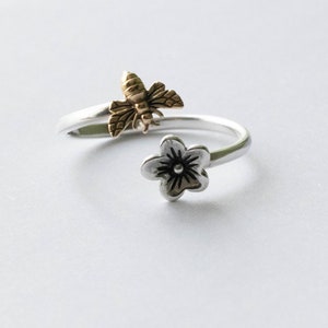 May include: A silver ring featuring a gold bee and a silver flower design.
