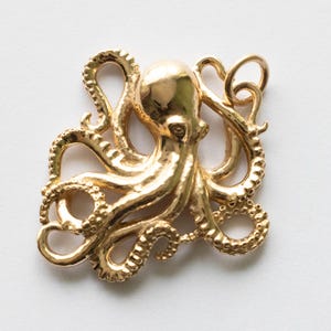 May include: A gold-coloured octopus pendant with detailed tentacles and a textured surface. The octopus is centred and appears to be made of metal. The pendant is a nautical-themed accessory.