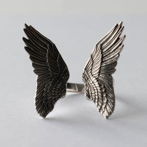 Peut inclure: Une bague en argent avec deux ailes d'ange de chaque c&ocirc;t&eacute;. Les ailes sont d&eacute;taill&eacute;es et ont une finition textur&eacute;e.
