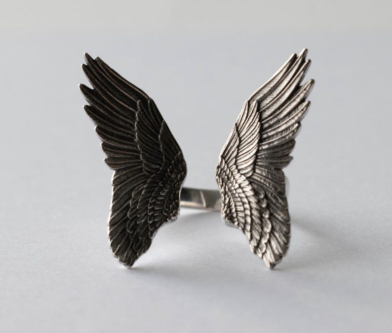 Peut inclure: Une bague en argent avec deux ailes d'ange de chaque c&ocirc;t&eacute;. Les ailes sont d&eacute;taill&eacute;es et ont une finition textur&eacute;e.