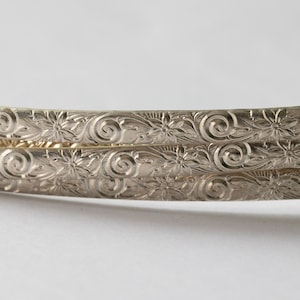 May include: Three silver bangles with an intricate floral and swirl design.