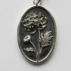 May include: A silver oval pendant with a detailed embossed design of a chrysanthemum flower.