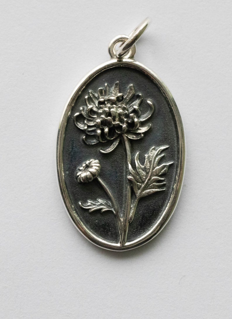 May include: A silver oval pendant with a detailed embossed design of a chrysanthemum flower.