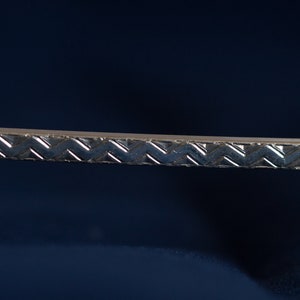 Könnte beinhalten: Nahaufnahme einer silbernen Metallverkleidung mit einem strukturierten, geflochtenen Muster.