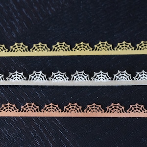 May include: Three strips of decorative trim with a spiderweb design. The top strip is gold, the middle strip is silver, and the bottom strip is copper.