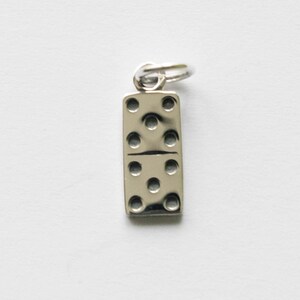 May include: A silver-coloured charm shaped like a domino, with seven circular indentations. The charm has a small loop at the top for attachment. The domino is a classic game piece.