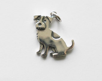 May include: A silver charm in the shape of a dog. The dog is sitting with its head turned to the side and its tail curled up.