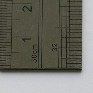 K&ouml;nnte beinhalten: Zwei silberfarbene Anh&auml;nger in Form eines Atoms. Die Anh&auml;nger haben einen Durchmesser von etwa 2,5 cm. Einer der Anh&auml;nger ist nach oben, der andere nach unten gerichtet. Ein Lineal ist zwischen den Anh&auml;ngern platziert und zeigt die Ma&szlig;e in Zentimetern an.