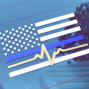 May include: A white and blue American flag with a thin blue line and a gold heartbeat graphic. The flag is on a blue background.