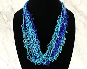 May include: A multi-strand beaded necklace with a graduated ombre design in shades of blue. The necklace is made of small, round beads and has a delicate, flowing look.