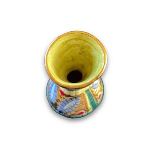 May include: A ceramic vase viewed from above, featuring a wide, circular opening with a pale yellow interior. The exterior surface is decorated with a repeating pattern of blue leaf-like shapes, red circular accents, and textured gold-toned details.