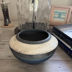 May include: A low, wide ceramic bowl with a textured finish. The rim is dark charcoal, followed by a wide band of off-white crackle glaze, and a base section featuring a gradient of dark gray to deep blue with a speckled, granular surface texture.