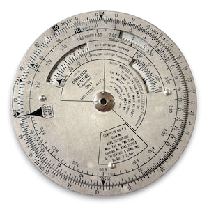 May include: A vintage circular aviation computer, featuring concentric scales and detailed markings for calculations. The device includes scales for speed, altitude, and temperature, with text indicating its purpose and manufacturer. The computer is made of metal and has a central pivot.