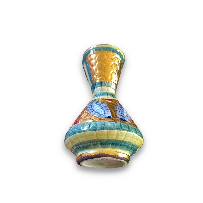 May include: A small ceramic vase with a flared neck and a wide, rounded base. The surface features a textured, honeycomb-like pattern in gold, accented by horizontal bands of teal and cream, and blue leaf-shaped motifs with small red details.