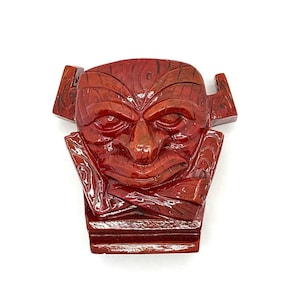 May include: A red wooden mask with intricate carvings and a fierce expression. The mask is mounted on a wooden base.