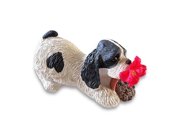 Pode incluir: Estatueta de cerâmica de um cão preto e branco em pose brincalhona, segurando uma flor vermelha vibrante na boca. O cão tem uma mancha preta na lateral. A flor vermelha adiciona cor à estatueta decorativa.