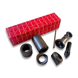 May include: A set of dark gray metal machine tool components including a cylindrical sleeve, a threaded bolt with a pointed tip, a small rod, and several rings, accompanied by a rectangular red box with the white text Sterrett printed repeatedly.