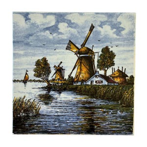 May include: A vintage Dutch tile depicting a picturesque scene of windmills, a canal, and a small village. The tile features a blue sky with white clouds, a canal with a sailboat, and two windmills with thatched roofs. The village is in the background, with a small house and a few trees.