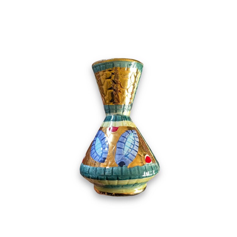 May include: A small ceramic vase with a flared neck and a wide base. The surface features a metallic gold finish with teal green accents, blue oval patterns, and small red dots. The neck has a textured gold pattern, and the base has a teal grid design.