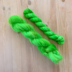 May include: Two skeins of bright green yarn. One skein is a fuzzy, mohair blend and the other is a smooth, single-ply yarn.