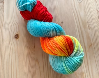 Hand dyed multicolored sock yarn, Light blue yarn with red, orange and yellow stripes - Arrullo | Assigned color pooling yarn