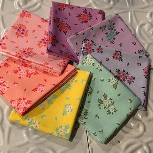 May include: A set of eight fabric squares with a floral pattern. The fabric squares are in various shades of pink, purple, yellow, and green.
