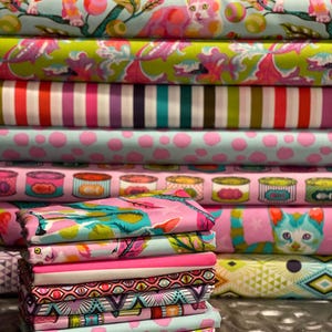 Pu&ograve; includere: Una pila di rotoli di tessuto colorati con vari motivi. I disegni includono gatti, strisce, pois e forme geometriche in tonalit&agrave; di rosa, verde, blu e viola. I tessuti sembrano essere di cotone o un materiale simile, adatti per progetti di cucito.