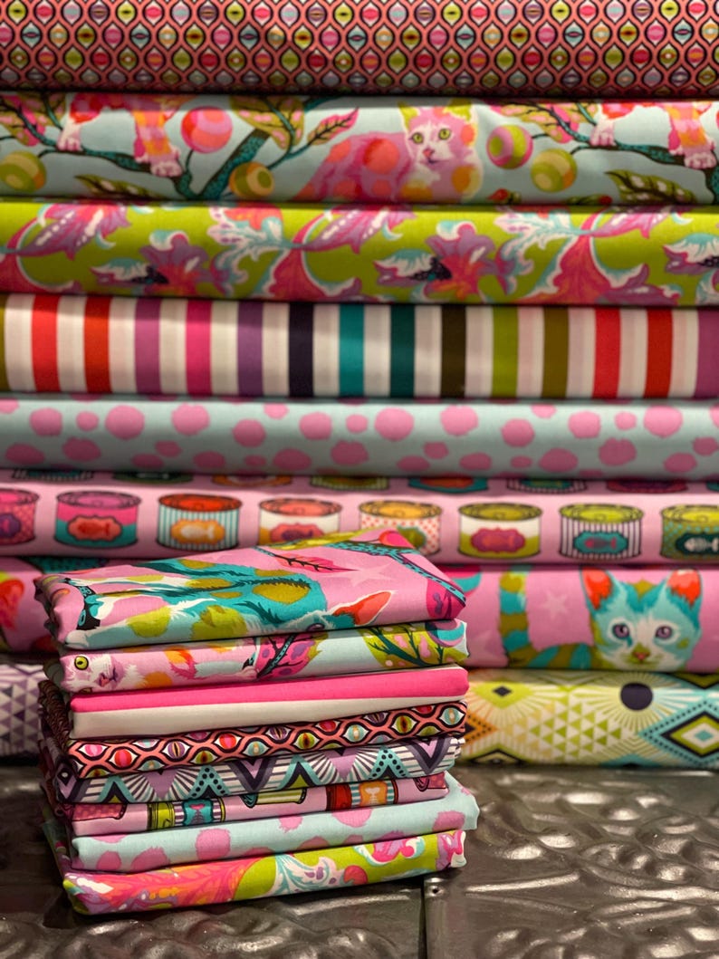Pu&ograve; includere: Una pila di rotoli di tessuto colorati con vari motivi. I disegni includono gatti, strisce, pois e forme geometriche in tonalit&agrave; di rosa, verde, blu e viola. I tessuti sembrano essere di cotone o un materiale simile, adatti per progetti di cucito.