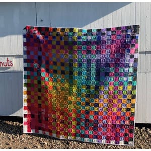 Puede incluir: Una colcha de retazos colorida con un patrón de cuadros. La colcha está hecha de cuadrados de diferentes colores y telas, incluyendo rojo, naranja, amarillo, verde, azul, morado y rosa. La colcha está acolchada con un patrón de puntadas simple.