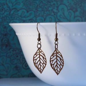 May include: A pair of bronze leaf-shaped earrings with delicate cutouts. The earrings hang from simple hooks.