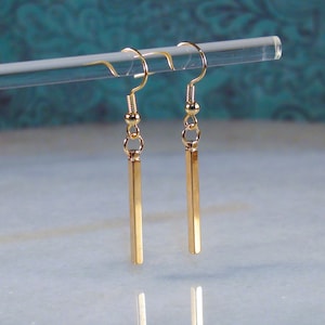 May include: A pair of gold-toned dangle earrings with a long, thin, rectangular bar pendant.