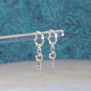 May include: A pair of silver key-shaped earrings with heart-shaped keyholes hanging from hoop earrings.